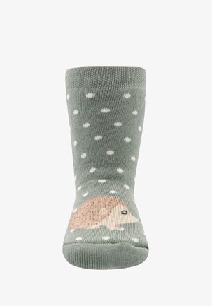 Grüne gestrickte Socken mit weißen Punkten und einem Cartoon-Igel-Design. Weicher Stoff, wadenlange Länge und gerippter Bund für einen guten Sitz.