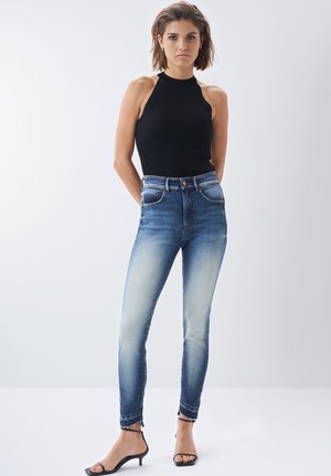 Hochtaillierte blaue Jeans aus Denim mit einem verblassten Finish, ausgestattet mit fünf Taschen, einem Reißverschluss und einem schmal zulaufenden Bein, kombiniert mit einem schwarzen gerippten Oberteil.