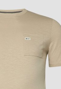 T-shirt beige en coton à manches courtes, col rond et petite poche poitrine avec une étiquette « 5.0 Elevated Casual ».