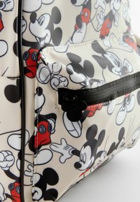 Sac à dos avec un extérieur crème à motifs présentant divers designs de Mickey Mouse. Comprend une fermeture zippée noire et un tirette en forme de Mickey.