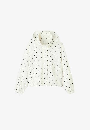 Veste blanche à capuche avec des pois noirs, fermeture éclair à l'avant, poignets élastiques et deux poches latérales.