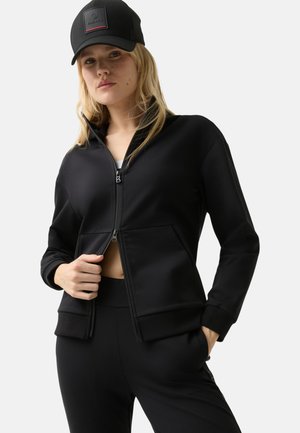 Black zip-up jacket made of smooth fabric, featuring a high collar, front pockets, and ribbed cuffs. Worn with matching black pants.