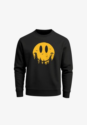 Schwarzer Pullover mit einem großen gelben Smiley-Gesicht-Design, das Bäume und Vögel integriert. Lange Ärmel und Rundhalsausschnitt.