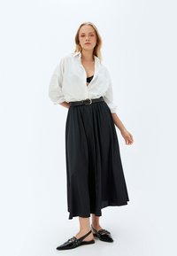 Weiße übergroße Bluse, schwarze plissierte Maxiröhre und schwarze Ballerinas mit dekorativen Akzenten. Glatter Stoff und entspannte Silhouette.