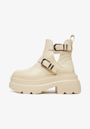 Smėlio spalvos stambūs Čelsio batai iš lygaus sintetinio materialo, su dviem juodais sagtimis, išpjautomis šoninėmis dalimis ir storu platforminiu padu.