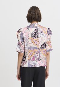 Blouse en soie avec manches bouffantes arborant un design patchwork en rose, noir et tons pastel, ornée de motifs paisley et floraux.