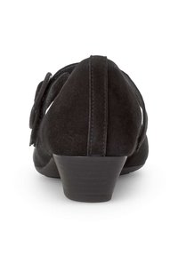 Talons en suédine noire avec un petit talon compensé texturé, présentant un design découpé et des accents en tissu décoratifs sur les côtés.