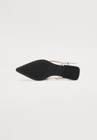 Chaussure noire à bout pointu avec une semelle lisse et des brides transparentes. Talon carré et bas pour plus de stabilité. Design minimaliste sans motifs.