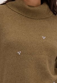 Olijfgroen gebreid trui met een hoge geribbelde kraag. Bevat drie kleine decoratieve kraaltjes aan de voorkant. Zachte textuur met een relaxte pasvorm.