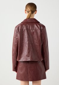 Bordeaux leren jack met een relaxte pasvorm, puntige kraag en zichtbare textuur. Heeft een cropped ontwerp, gecombineerd met een bijpassende rok.