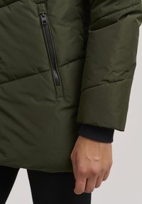 Olive green puffer jacket featuring a side zipper, quilted design, and ribbed cuffs, showcasing a smooth texture and lightweight appearance.