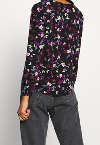 Blouse à manches longues florale avec un fond noir et des fleurs roses, violettes et bleues. Le tissu est léger et a une coupe décontractée.