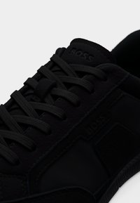 Baskets en cuir noir et tissu avec lacets ronds noirs et logo "BOSS" embossé sur la languette et le côté.