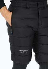 Zwarte gewatteerde shorts van nylon met een logo, een ritszak en een elastische tailleband. Kenmerkt zich door een gewatteerde textuur en een taps toelopend ontwerp.