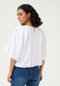 Hvid, kortærmet bluse med løs pasform, detalje med nøglehul i ryggen og struktureret stof. Sammen med mid-rise blå denim jeans.