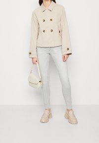 Chaqueta beige de doble botonadura con grandes botones, jeans ajustados gris claro, mocasines de plataforma beige y un pequeño bolso crema.