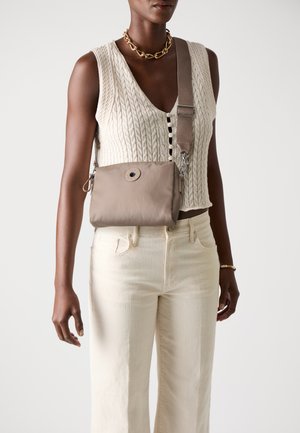 Borsa a tracolla beige in tessuto liscio, con dettaglio di bottone rotondo, tracolla regolabile e accessori in metallo argentato. Indossata sopra un top strutturato.