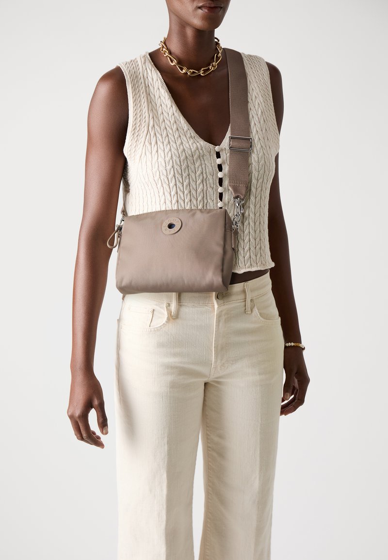 Borsa a tracolla beige in tessuto liscio, con dettaglio di bottone rotondo, tracolla regolabile e accessori in metallo argentato. Indossata sopra un top strutturato.