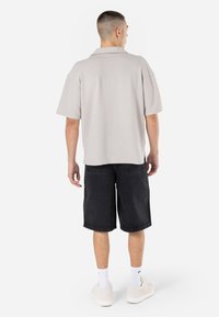 Cămașă scurtă, texturată, gri deschis, cu un croi lejer, purtată cu pantaloni scurți din denim negri. Asortată cu adidași albi și șosete până la glezne.