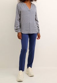 Luftig bluse med lange ærmer i hvidt og navy zigzag-mønster, kombineret med blå slim-fit bukser og beige sneakers.