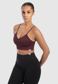 Top corto de canalé burdeos con tirantes finos, combinado con leggings negros de cintura alta que presentan una discreta etiqueta de marca. Textura suave en toda la prenda.