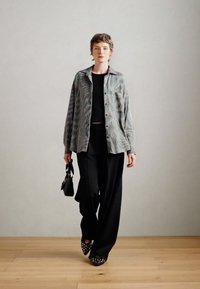 Camicia multicolore con bottoni e strisce verticali, top nero, pantaloni larghi neri e borsa nera. Tessuto strutturato e vestibilità ampia.