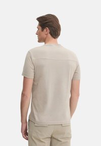 Camiseta de manga corta y cuello redondo en color beige claro, que presenta una textura suave y un diseño minimalista con un detalle de costura horizontal en la parte posterior.