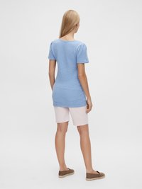 Top texturizado azul claro com mangas curtas em balão, combinado com calções rosa claro. Modelo usa sapatos slip-on castanhos.