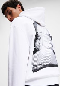 Weißer Baumwoll-Hoodie mit grafischem Druck auf der Rückseite, schwarz-weiß gestreiftem Design und "Karl Lagerfeld"-Textdetail.
