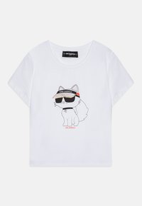 Bílý bavlněný tričko s potiskem kreslené lišky, která nosí sluneční brýle a kšiltovku, s nápisem "KARL LAGERFELD" v červené barvě níže.