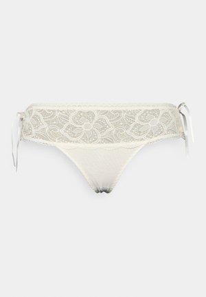 Tanga de renda em creme com padrões florais e laços laterais de cetim; apresenta bordas rendadas e um painel frontal suave e transparente.