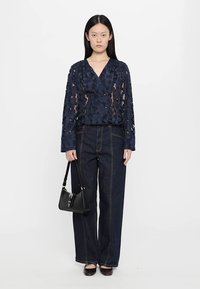 Navy floral lace blouse with long sleeves and double-breasted design, paired with high-waisted dark denim wide-leg jeans and a black handbag.
