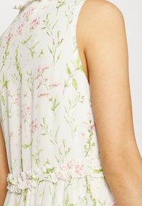 Abito senza maniche a fiori con sfondo bianco, caratterizzato da stampa botanica verde e rosa, dettaglio in rouches in vita e una morbida texture del tessuto.