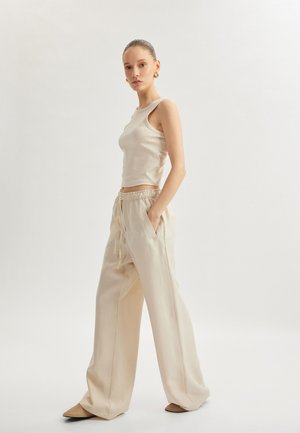 Top de tirantes acanalado color crema combinado con pantalones sueltos de cintura ajustable. Tejido suave, piernas anchas y zapatos planos beige.