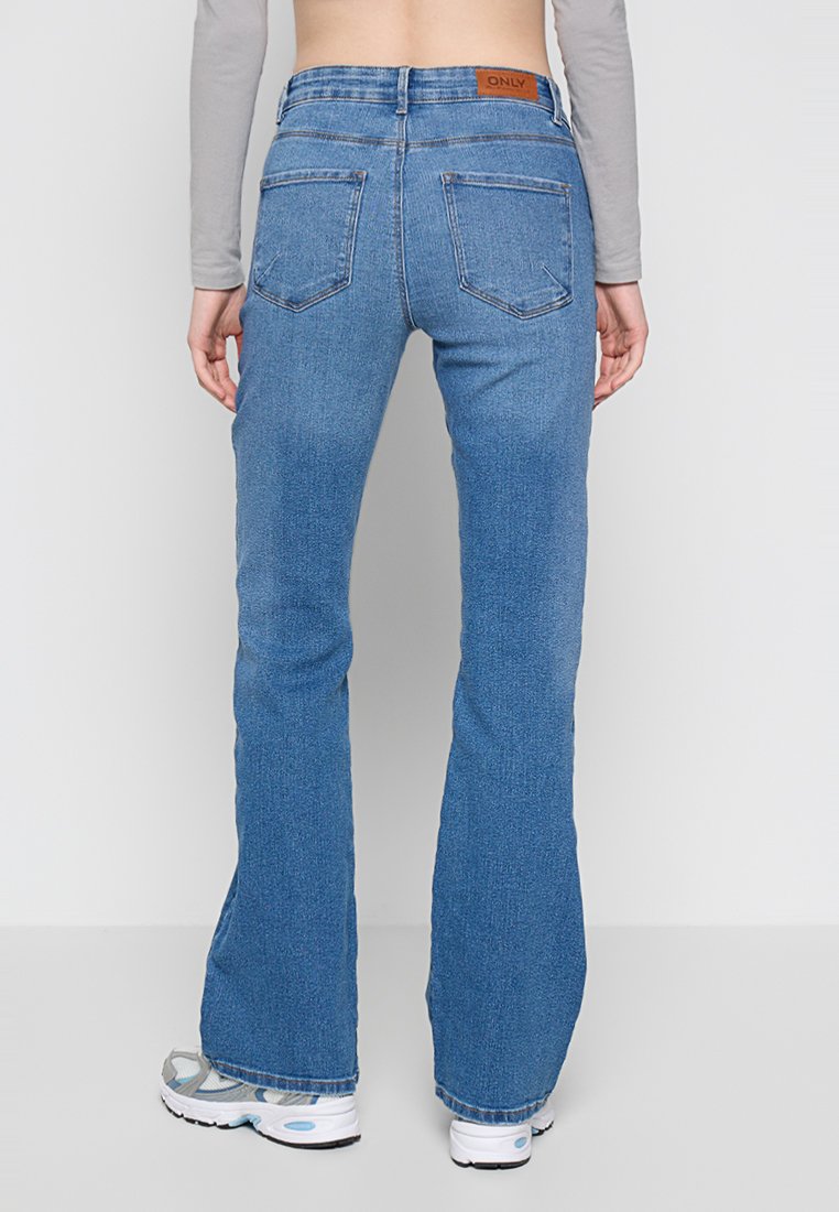 Ausgestellte blaue Jeans aus Denim mit einem braunen Lederpatch an der Taille. Verfügt über ein Fünf-Taschen-Design und eine strukturierte Oberfläche.