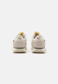 Les chaussures présentent un design beige et vert avec une tige en daim et en maille, une semelle texturée et un accent jaune le long du col.