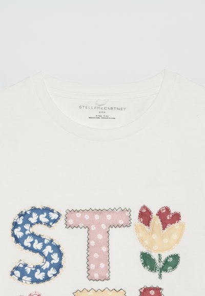 Λευκό παιδικό t-shirt με πολύχρωμα λουλουδάτα και διακοσμητικά γράμματα κεντημένα με πατσγουόρκ που σχηματίζουν το "STELLA" κοντά στη λαιμόκοψη.