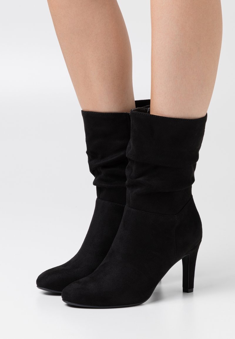 Botines de ante negros con un diseño arrugado, punta afilada y tacón apilado. Presentan una textura suave y sin herrajes o patrones visibles.