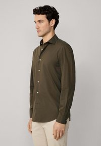 Camisa de manga larga en verde oliva, hecha de una tela suave, que presenta un cuello abotonado y botones blancos en la parte frontal.