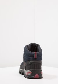 Dunkelblaue Wanderschuhe mit einer strukturierten Oberseite, gepolstertem Schaft und grauer Gummisohle, die rote Akzente und Grip-Muster aufweist.
