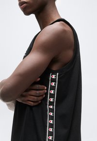 Άτομο που φοράει μαύρο αμάνικο αθλητικό φανελάκι με λογότυπα Champion στο πλάι, με τα χέρια σταυρωμένα στο στήθος.