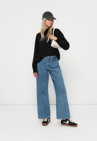 Svart genser, blå vide jeans, svarte sneakers med hvite detaljer, grå caps og en liten kremfarget håndveske. Enkelt, uformelt antrekk.