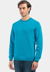 Maglione a maniche lunghe azzurro chiaro con scollo rotondo e accenti neri. Presenta un logo discreto sul petto. Texture morbida, vestibilità casual.