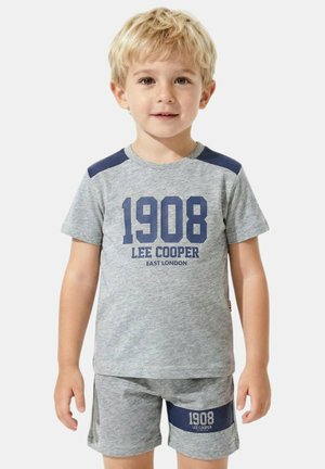 Jeune garçon aux cheveux blonds portant un ensemble t-shirt et short gris Lee Cooper assorti avec un texte bleu "1908" et des accents aux épaules.