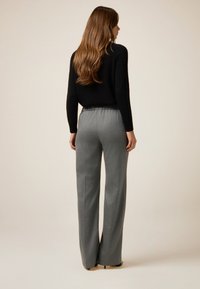 Pantalones grises de pierna ancha con una tela texturizada y una cinturilla elástica, combinados con un suéter negro ajustado, vistos desde la parte posterior.