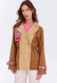 Dvojfarebná bunda v hnedej a béžovej farbe, s károvanými akcentmi na golieri a manžetách, s vypasovaným pásom a veľkými gombíkmi.