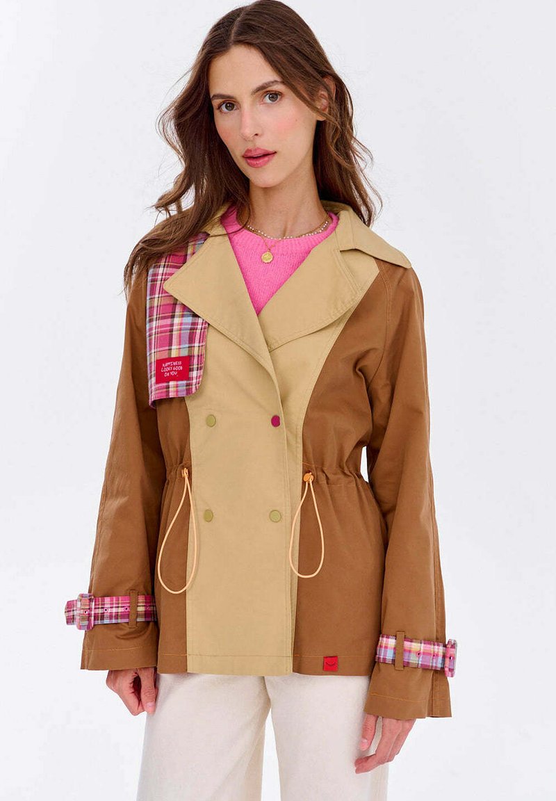 Dvojfarebná bunda v hnedej a béžovej farbe, s károvanými akcentmi na golieri a manžetách, s vypasovaným pásom a veľkými gombíkmi.