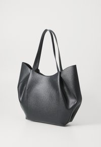 Zwarte leren totebag met twee schouderbanden en een rechthoekige gestikte detail aan de voorkant, staand op een witte ondergrond.
