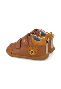 Zapatos de cuero marrón con correas de velcro, que presentan un diseño de cara de oso en el lateral, y una suela de goma suave. Acentos de ante marrón texturizado.