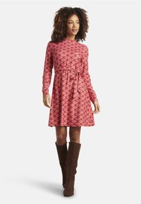Red patterned dress with long sleeves, belted waist, and flared skirt. Paired with knee-high brown suede boots. Smooth fabric texture.